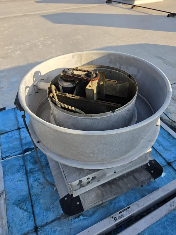 Technician servicing a commercial kitchen exhaust fan motor and belt on a rooftop unit